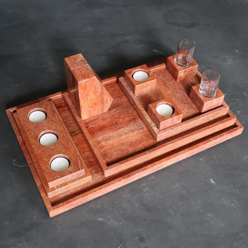 May include: A rectangular, reddish-brown wooden tray with multiple compartments. It features three candle holders, two small platforms holding shot glasses, and a central geometric structure. The tray is designed for decorative use.