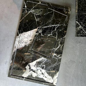 Könnte beinhalten: Ein Satz von drei rechteckigen Serviertabletts aus schwarzem Marmor mit weißen Adern. Die Tabletts sind ineinander verschachtelt, mit einem großen Tablett, einem mittleren Tablett und einem kleinen Tablett. Der Marmor hat eine polierte Oberfläche und einen gerahmten Rand.