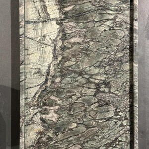 May include: Rectangular serving tray with a natural stone appearance. The tray features a dark gray border and a surface with a swirling pattern of gray, green, and black tones. The tray's design evokes a sense of organic elegance.