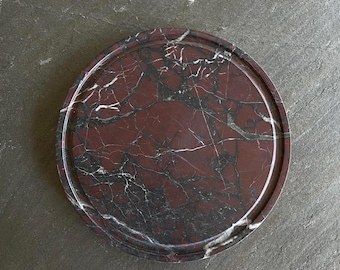 May include: A round, red and black marble serving tray with a raised edge. The tray has a natural, polished finish.
