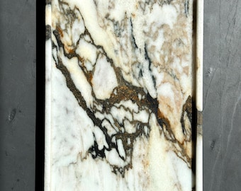 May include: A white marble serving tray with black and gold veining. The tray has a raised edge and is perfect for serving snacks or drinks.