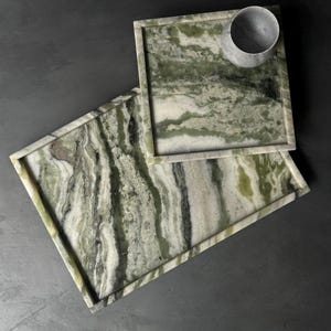 May include: Two green and white marble trays with a decorative border. The smaller tray is on top of the larger tray.