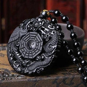 May include: Black obsidian necklace with a round pendant featuring a yin yang symbol surrounded by a dragon and phoenix design.
