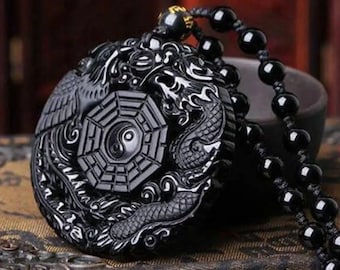 Puede incluir: Collar de obsidiana negra con un colgante redondo que presenta un símbolo yin yang rodeado por un diseño de dragón y fénix.