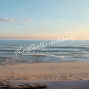 May include: A view of the ocean from a window with white curtains. The ocean is blue and the sky is light blue. The sand is light brown. The window is open and the curtains are pulled back.