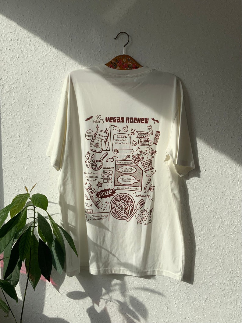 Weißes oversized T-Shirt mit braunem Backprint. Vegan Kochen im retro Cartoon style, unisex