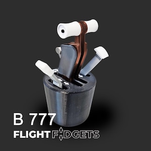 Może przedstawiać: Czarny i brązowy model kwadrantu przepustnicy z białymi dźwigniami i uchwytami. Model zawiera biały tekst "B 777" i "FLIGHT FIDGETS". Tło jest ciemnoszare.