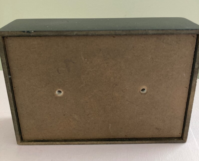 May include: A small, rectangular, black wooden box with a light brown back panel. The back panel has two holes. The box appears to be empty. The box is likely used for storage or display.