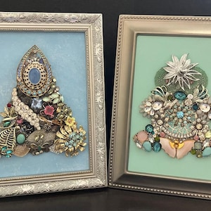 May include: Two framed Christmas trees made of rhinestones and other jewelry. The tree on the left is on a light blue background and the tree on the right is on a light green background.