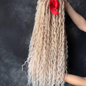 May include: Long blonde ombre synthetic dreadlocks with a red ribbon tied at the top.