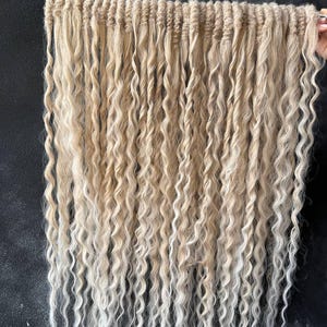 May include: A set of blonde and white ombre hair extensions with a wavy texture. The extensions are arranged in rows and are ready to be used for braiding or weaving.