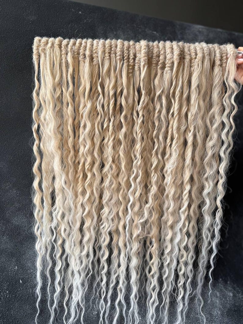 May include: A set of blonde and white ombre hair extensions with a wavy texture. The extensions are arranged in rows and are ready to be used for braiding or weaving.