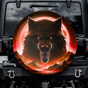 May include: A spare tire cover featuring a snarling wolf with glowing eyes against a red moon backdrop. The design includes a mountain range silhouette at the bottom, with a dark sky in the background. The cover is mounted on a black vehicle.