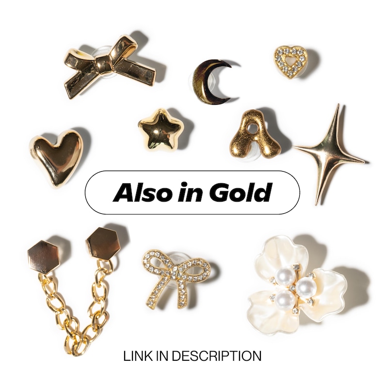 May include: A collection of gold-colored earrings in various shapes, including a bow, heart, star, crescent moon, and a four-pointed star. Some earrings are embellished with rhinestones or pearls. The text "Also in Gold" and "LINK IN DESCRIPTION" are also visible.