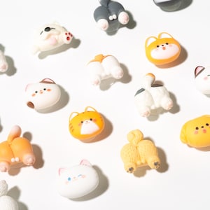 以下が含まれることがあります： さまざまな動物をテーマにした装飾用マグネットのコレクション。マグネットは、白、オレンジ、黄色など、さまざまな色で、猫、犬、その他の動物の漫画風のデザインが特徴です。マグネットは白い表面に配置されています。