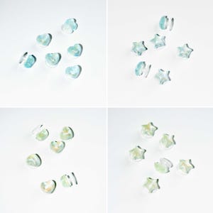 Op de afbeelding: Doorzichtige oorbellen in hart- en stervorm met een blauw-groen marmereffect. Ze worden gepresenteerd op een witte achtergrond, waardoor hun doorschijnende kwaliteit en unieke ontwerp worden benadrukt.