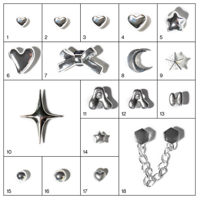May include: A collection of silver-toned charms in various shapes, including hearts, stars, bows, moons, and letters. The charms are arranged on a white surface, showcasing their reflective qualities. Ideal for jewelry making or craft projects.