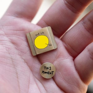 May include: A small, tan square with the words "YOUR Life" and a pie chart with a yellow section. A small, round, gold-coloured object with the words "THIS MOMENT" is also present.