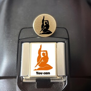 May include: A circular gold-toned pin featuring a black silhouette of a person in a yoga pose, positioned above a rectangular silver-toned charm with a white background, an orange silhouette of the same yoga pose, and the black text You can.