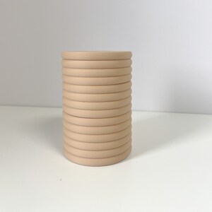 May include: A stack of beige round coasters. The coasters are made of a smooth material and are stacked on top of each other.