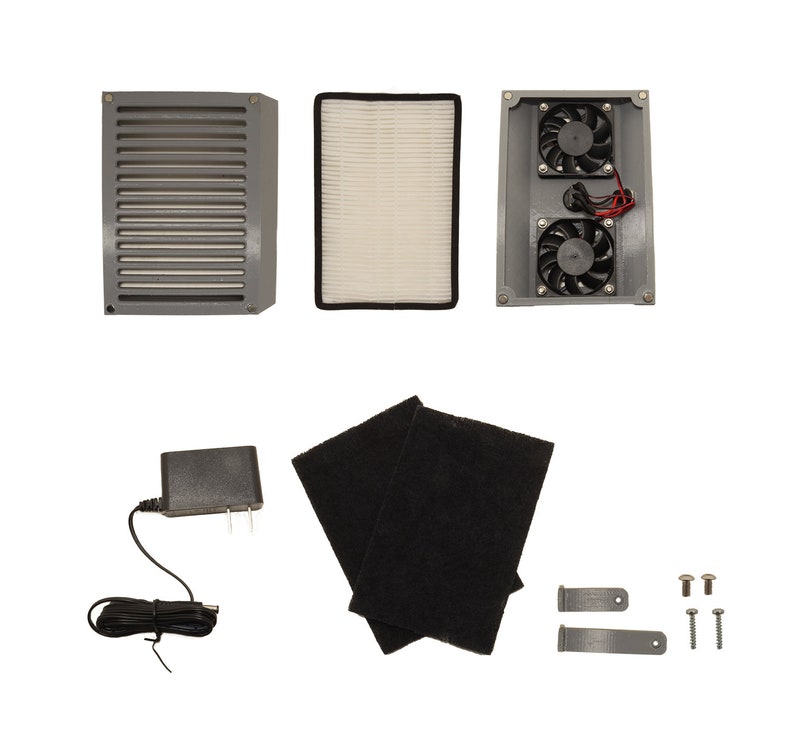 May include: A set of air purifier parts including a grey air filter housing, a white air filter, a grey housing with two fans, a black carbon filter, a power adapter, two grey brackets, and four screws.
