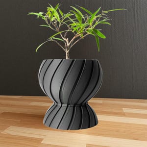 May include: A black, swirl-patterned ceramic planter with a plant inside. The planter has a wide base and a narrow neck.