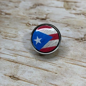 May include: A round, silver-colored pin with a red, white, and blue Puerto Rican flag design.