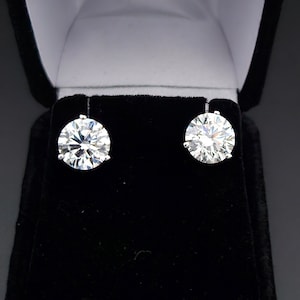 May include: A pair of round, clear diamond stud earrings in a black velvet jewelry box.