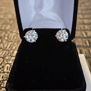 May include: A pair of round, clear, diamond earrings in a black velvet jewelry box.