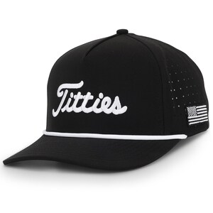 May include: Black baseball cap with the word "Titties" in white script across the front. The cap has a white rope detail and a small American flag patch on the side. The cap has a curved brim.