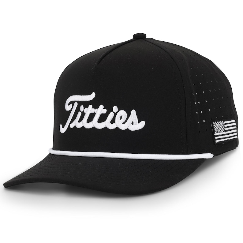 May include: Black baseball cap with the word "Titties" in white script across the front. The cap has a white rope detail and a small American flag patch on the side. The cap has a curved brim.