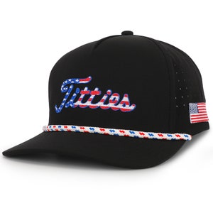 May include: Black baseball cap with the word "Titties" embroidered in red, white, and blue, with an American flag patch. The cap features a white, red, and blue rope detail along the brim.