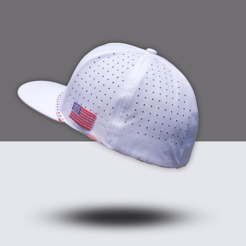May include: White baseball cap with a perforated design and a small American flag patch. The cap has a curved brim and a button on top. The brim has a red, white, and blue striped design.