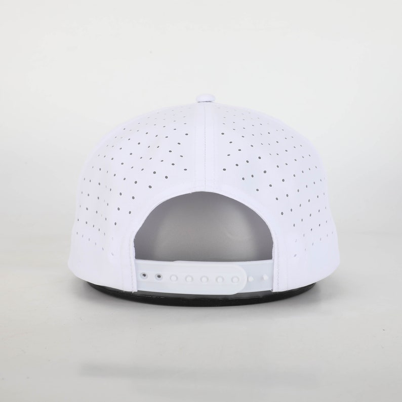 May include: White baseball cap with a perforated design for breathability. The cap features a curved brim and an adjustable strap at the back for a custom fit. The hat is a classic accessory for sun protection and casual wear.