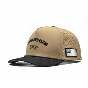 Puede incluir: Gorra de golf beige y negra con el texto "Curves and Clubs Golf Co. Est. 2024". La gorra presenta una visera negra, un parche con la bandera estadounidense en blanco y negro y un panel lateral perforado.