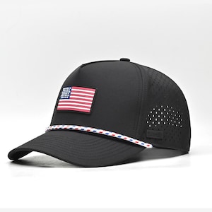 May include: Black baseball cap featuring an American flag patch. The cap has a perforated side panel and a white, red, and blue rope detail. The cap is a classic style with a curved brim.