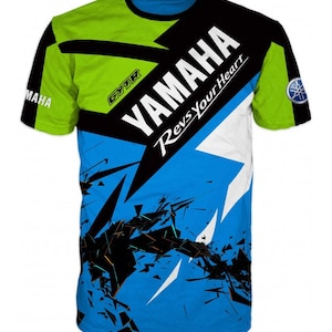 Op de afbeelding: Een blauw, groen, zwart en wit T-shirt met een grafisch ontwerp met het Yamaha-logo en de tekst "Revs Your Heart".