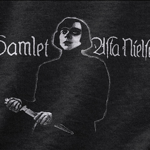 May include: Black and white graphic featuring a portrait of a person holding a dagger, with the text "Hamlet Alfa Nielsen" in a stylized font. The image has a textured appearance, suggesting a print or fabric.