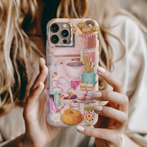 May include: A pink iPhone case with a colorful illustration of baking supplies, including a mixer, a bowl, a rolling pin, and various pastries. The case features the word "Flour" in a pink font.