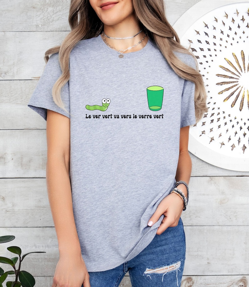以下が含まれることがあります： 緑の虫と緑のグラスが描かれたグレーのTシャツ。Tシャツには「Le ver vert va vers le verre vert」と書いてあります。