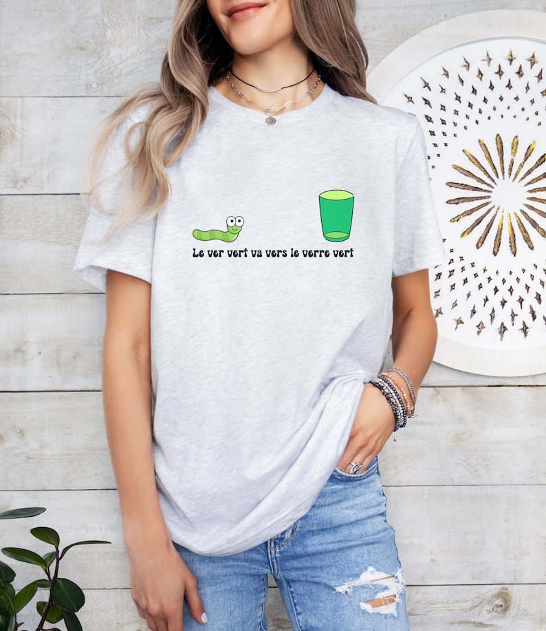 以下が含まれることがあります： 緑色の虫と緑色のグラスが描かれた灰色のTシャツ。Tシャツには「Le ver vert va vers le verre vert」という文字が書かれています。