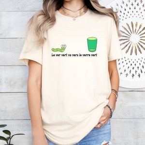 以下が含まれることがあります： クリーム色のTシャツに、緑色のミミズと緑色のグラスが描かれています。Tシャツには「Le ver vert va vers le verre vert」と書いてあります。