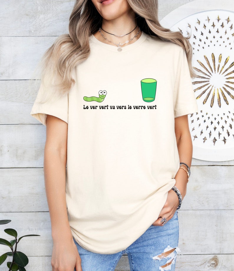 以下が含まれることがあります： クリーム色のTシャツに、緑色のミミズと緑色のグラスが描かれています。Tシャツには「Le ver vert va vers le verre vert」と書いてあります。