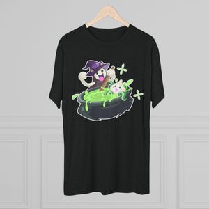 Puede incluir: Camiseta gris oscuro con un diseño de Halloween. El diseño muestra un fantasma con un sombrero de bruja removiendo un caldero de líquido verde con un gato dentro. Signos de suma blancos en el fondo.