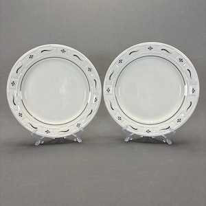 May include: Two round white ceramic plates featuring a dark green decorative border. The rim of each plate is embossed with a repeating pattern of small floral motifs and curved lines, complemented by a thin dark green circular line.
