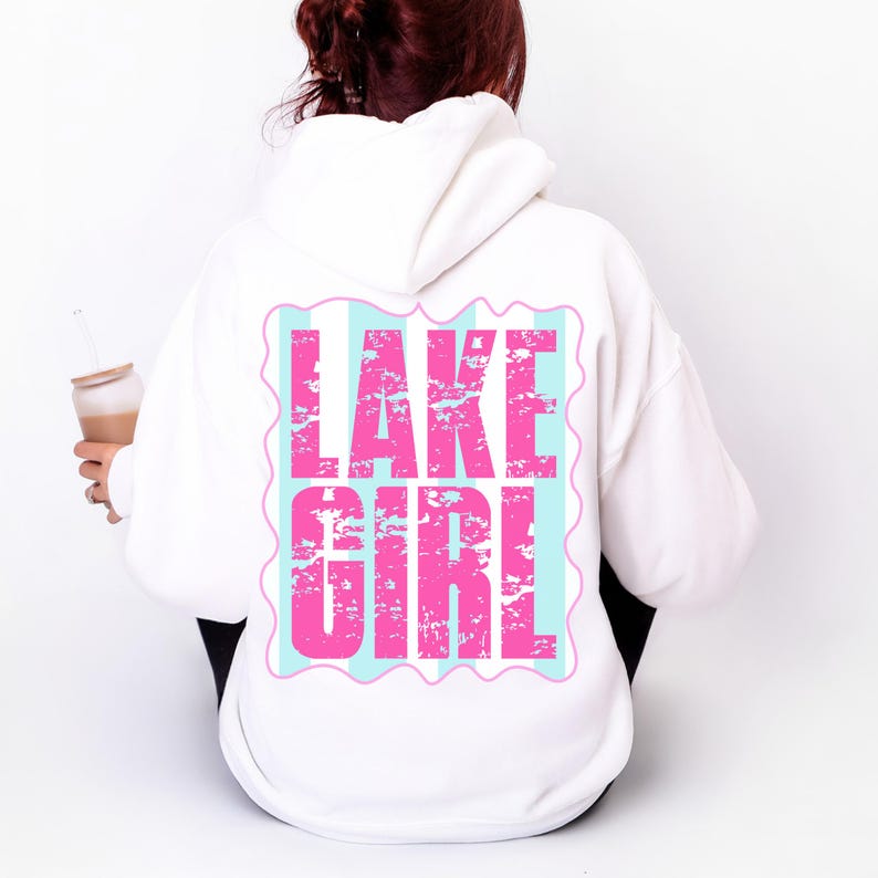 Puede incluir: Sudadera con capucha blanca con el texto "LAKE GIRL" en letras rosas desgastadas sobre un fondo a rayas azul claro y blanco. La sudadera tiene capucha y mangas largas. El tema general es ropa casual.