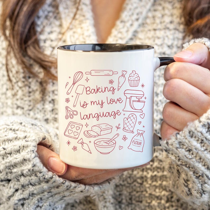 Może przedstawiać: Biały ceramiczny kubek z czarną obw&oacute;dką i uchwytem, z napisem "Baking is my love language". Kubek jest ozdobiony czerwonymi rysunkami narzędzi i smakołyk&oacute;w do pieczenia.