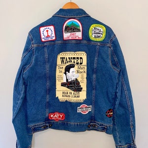 Könnte beinhalten: Eine blaue Jeansjacke mit verschiedenen Patches, darunter ein Fahndungsplakat für "The Man in Black" mit einem Zug, ein Patch mit der Aufschrift "The Katy Railroad" und ein Patch mit der Aufschrift "North Western System".