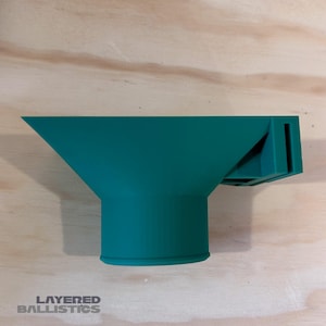 May include: A green plastic funnel with a rectangular opening at the top and a round opening at the bottom. The funnel is designed to be used with a reloading press.