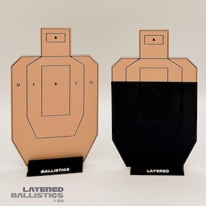 May include: Two target practice silhouettes. One is tan with black lines and the other is black. Both have a rectangular head and a rectangular base. The tan target has the word "BALLISTICS" on the base. The black target has the word "LAYERED" on the base.